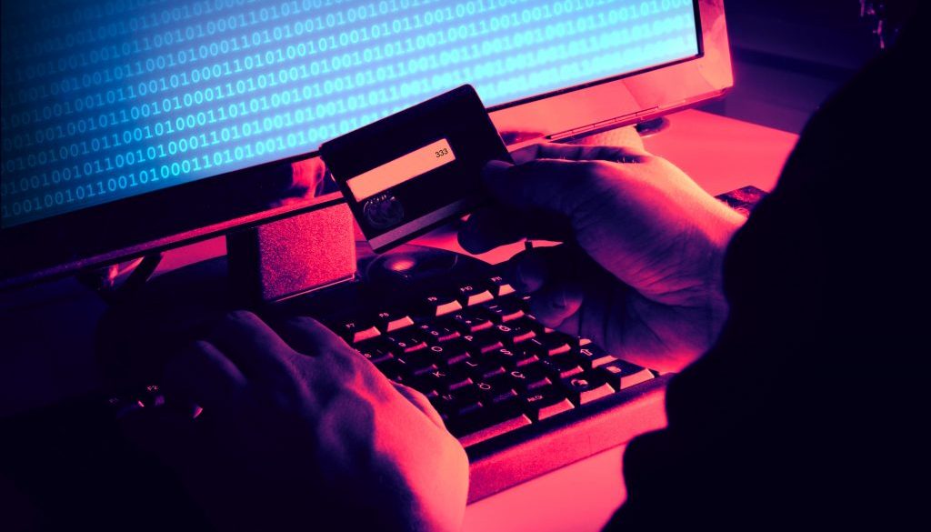 Black hands of anonymous hackers holding credit card and using, typing code on keyboard of laptop for remotely reach, receiving personal information online, Networking Crime Payment Security Concept