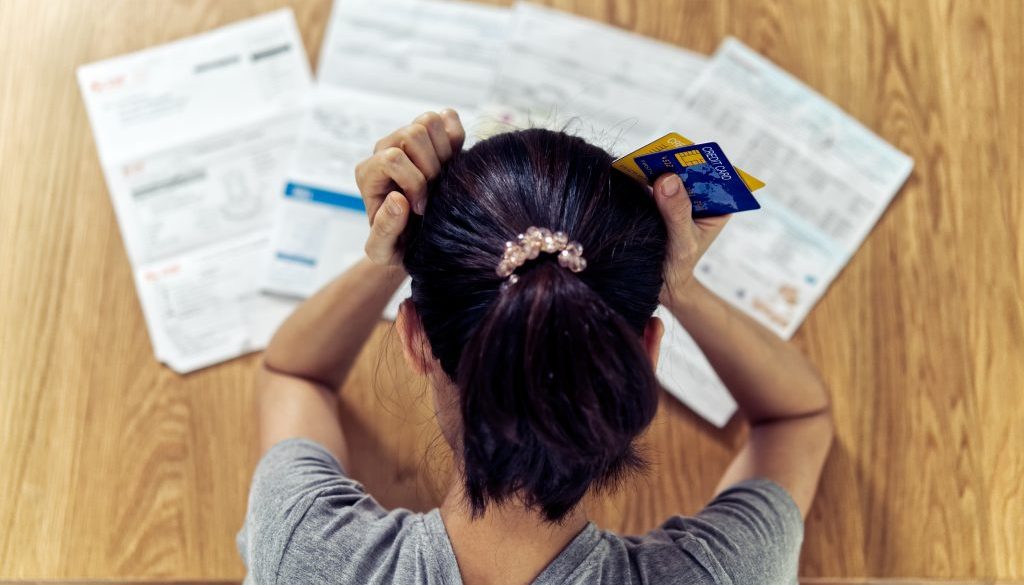 Top view of stressed young sitting Asian woman hands holding the head worry about find money to pay credit card debt and all loan bills. Financial problem concept.