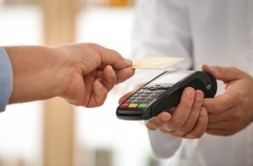 Customer using terminal for contactless payment with credit card in pharmacy, closeup