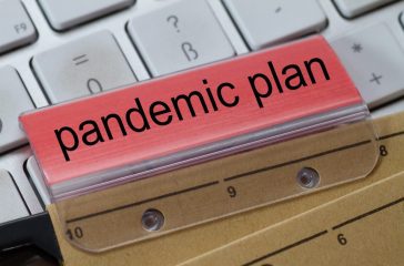 The words  pandemic plan can be seen on the label of a brown hanging folder. The hanging folder is on a computer keyboard.