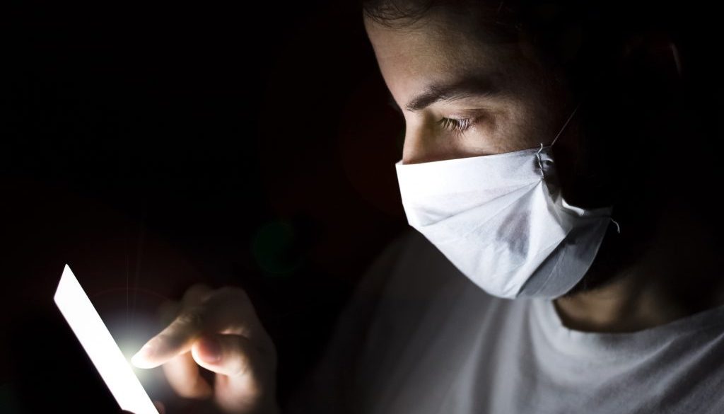 Close up of Young Man use Smart Phone at Night with Mask. Coronavirus.