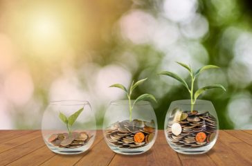 Saving money concept. Coins in glass jar. Investment money concept. Growing Money, finance and investment concept  background. Coins in three glass jar on wooden table with light and nature background