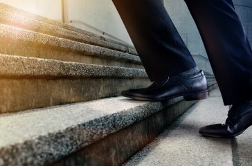 Motivation and challenging Career Concept. Steps Forward into a Success. Low Section of Businessman Walking Up on Staircase. Male in Black Formal Dress