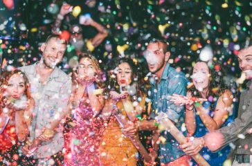 Happy friends doing party throwing confetti in the club - Millennials young people having fun celebrating in the nightclub - Nightlife, entertainment and festive holidays concept - Focus on man hand