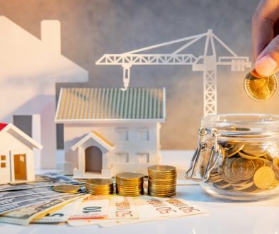 Real estate or property development. Construction business investment. Home mortgage loan rate. Hand putting coin in currency glass jar with Coin stack, banknotes, house and crane models on the table.