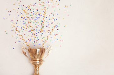 Trophy and confetti on light background, top view with space for
